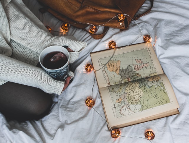 woman sitting on a bed with a cup of tea and fairy lights looking at a map in a book