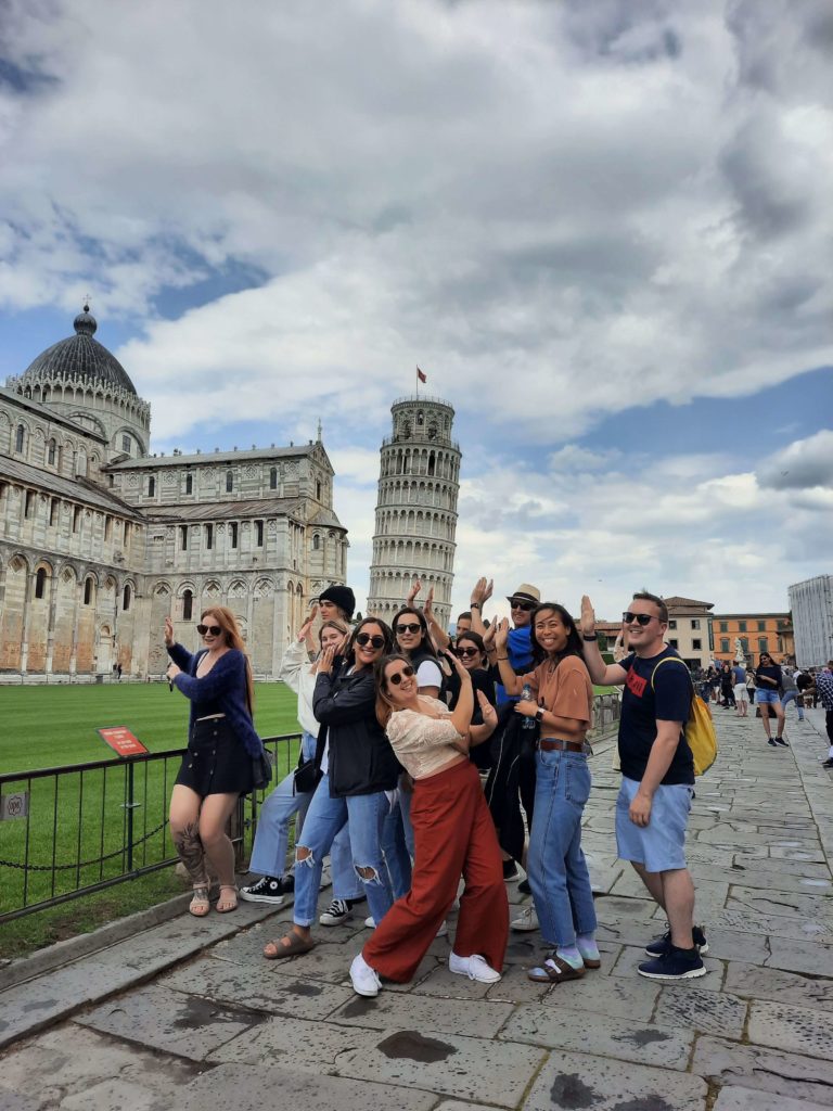 Group of young adults posing together in front of the Tower of Pisa. 