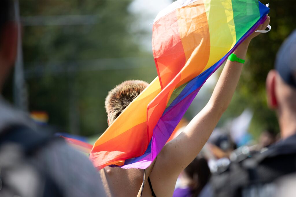 Young person holding up Pride flag, image taken from behind
