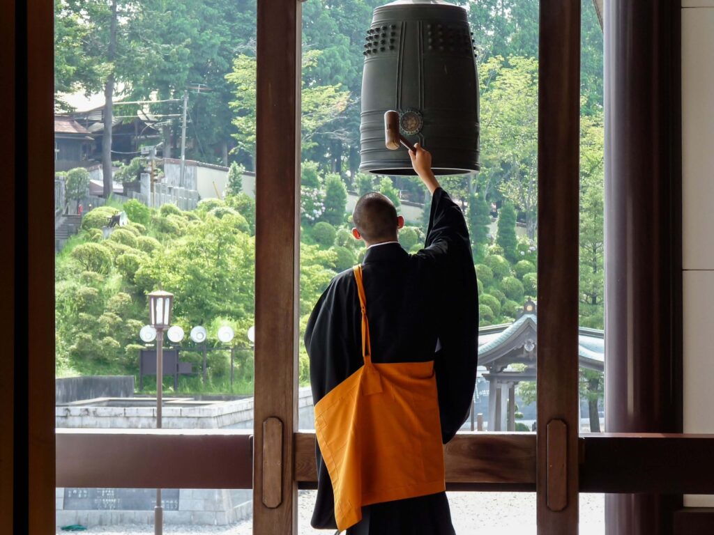 Japanese Buddhist in traditional robes, banging mallet against Bonshō (Buddhist bell)