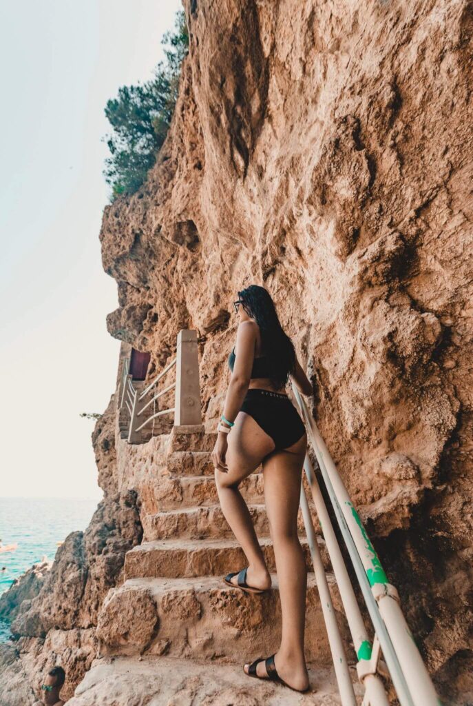 Young woman in a black bikini walking up cliffside steps in Dubrovnik, Croatia