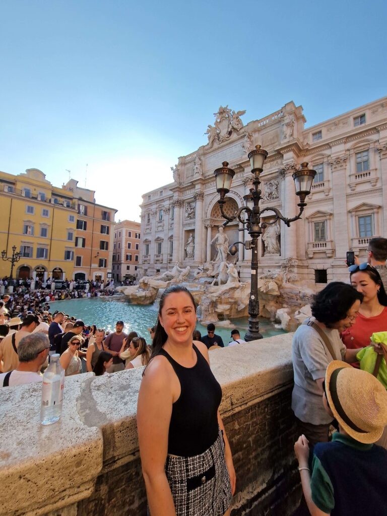 Young woman standing in front of Trevi Fountain smiling at camera