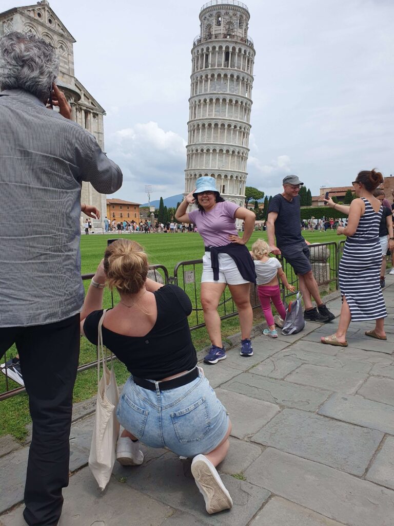 Young woman in bucket hat and lilac t-shirt posing in front of the Leaning Tower of Pisa