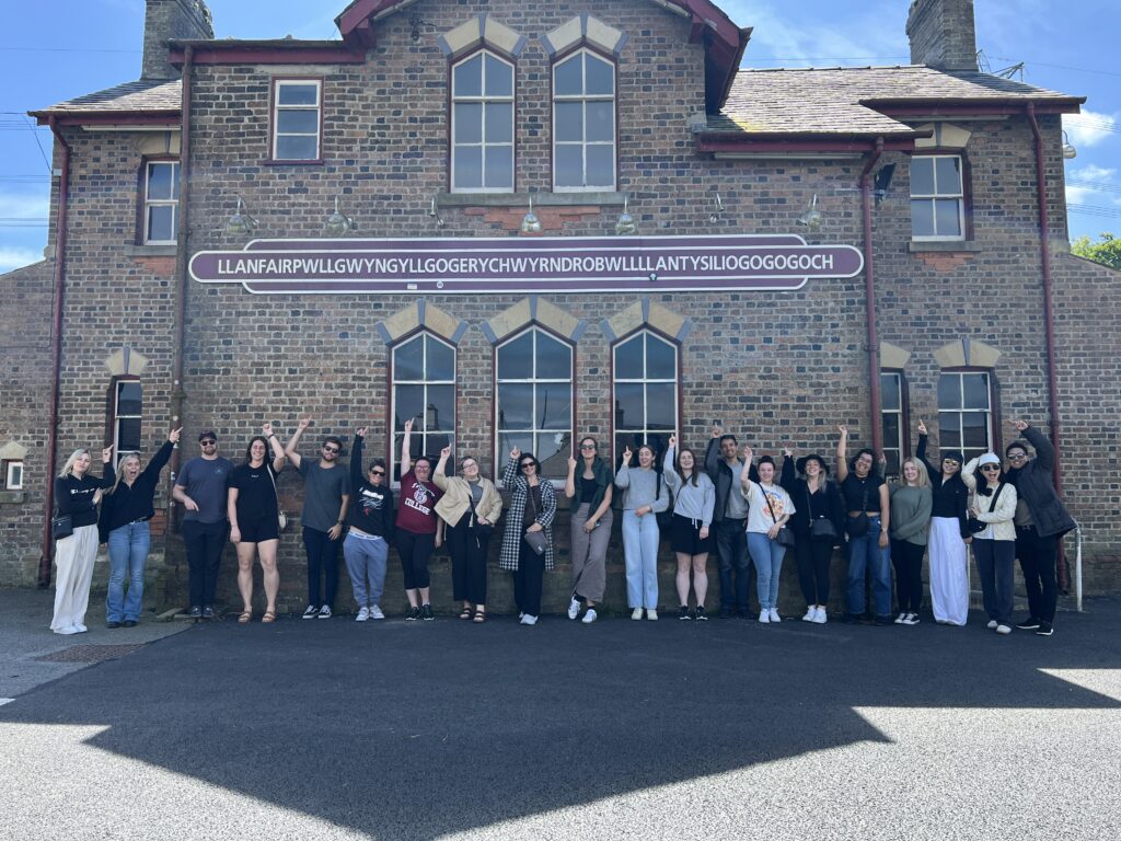 Group of travellers posing in front of place name sign in Wales